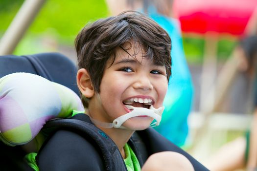 Handsome disabled eight year old biracial boy smiling and relaxing in wheelchair