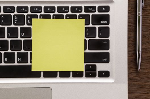 Blank yellow notepad putting on laptop keyboard with pen on wood table