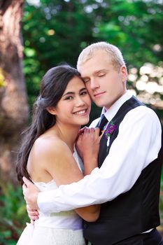 Caucasian groom holding his biracial bride, smiling. Diverse couple.