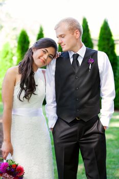 Caucasian groom holding his biracial bride, smiling. Diverse couple.