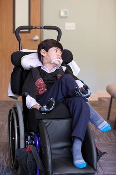 Handsome disabled eight year old biracial boy smiling and relaxing in wheelchair