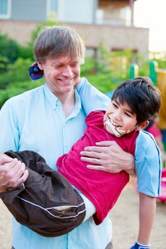 Caucasian father carrying biracial disabled son on playground