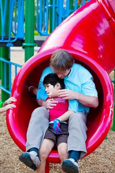 Caucasian father helping disabled son down slide at playground