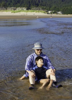 Caucasian father playing in water on beach with disabled son