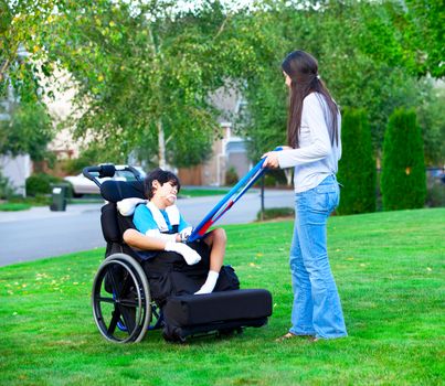 Biracial older sister playing outdoors with disabled little brother in wheelchair