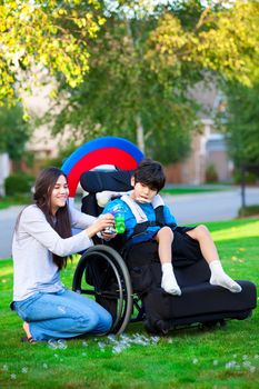 Biracial older sister playing outdoors with disabled little brother in wheelchair