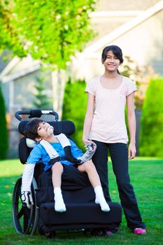 Disabled little boy in wheelchair with sister on grassy lawn outdoors