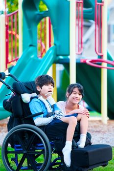 Sister sitting next to disabled brother in wheelchair at playground