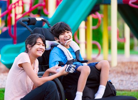 Sister sitting next to disabled brother in wheelchair at playground