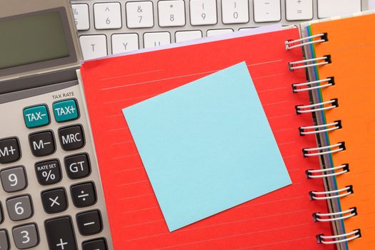 Blue blank notepad on colorful paper book with keyboard and calculator on background