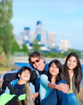 Disabled boy in wheelchair with family outdoors on sunny day, with city skyline in background