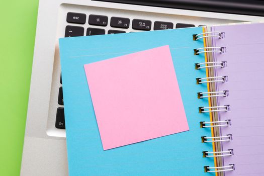 Pink blank notepad on colorful paper book with laptop on background