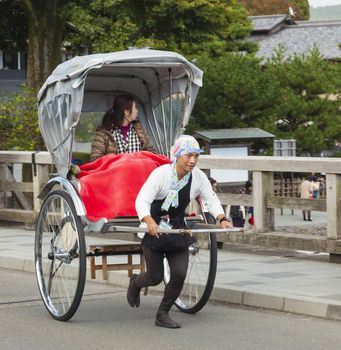 Osaka, Japan - Nov 3: Tourist riding a rickshaw in Arashiyama, a tourist district in Kyoto on Nov 3, 2014. Rickshaw is a popular mode of transportation in Japan in the 19th century. Rickshaw's popularity has declined by the 1930s but they can still be found in some tourist areas in Kyoto and Tokyo.The rickshaw runners also work as tourist guides, who take their clients to tourist spots.