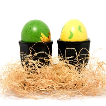 Two painted easter eggs in holders ans straw over white background