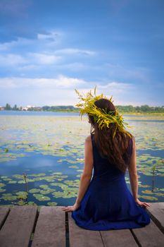girl by the lake with a wreath on head. Blue sky. Back view