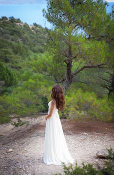 beautiful girl wearing white flowy dress in forest. Back view