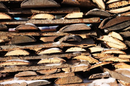 Background of stacked firewood in woodpile powdered white snow