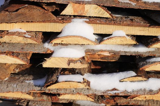 Background of stacked firewood in woodpile powdered white snow