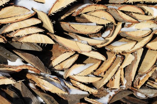 Background of stacked firewood in woodpile powdered white snow