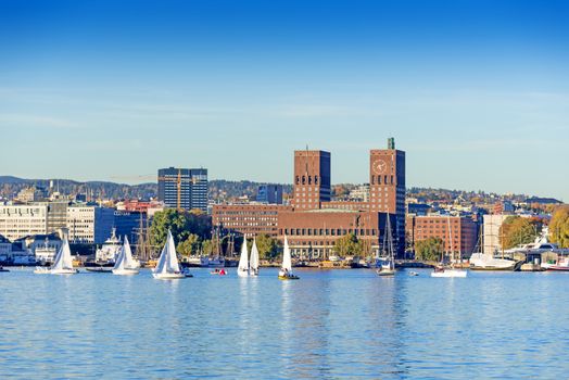 Harbour with boats and wooden yacht with town hall on background at sunset in Oslo, Norway