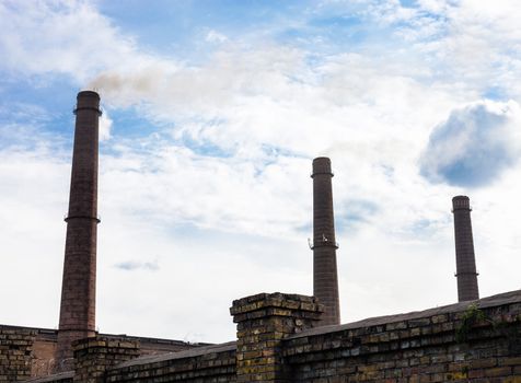 Three smoke stacks of the industrial plant against the cloudy sky