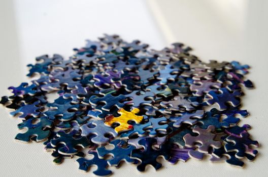 One yellow puzzle piece among a collection of blue puzzles pieces