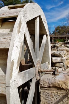 A weathered water wheel stands stationary amid a rock wall and blue sky