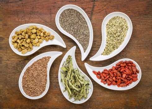 superfood samples  (mulberry, chia seeds, hemp seeds, goji berry, stevia leaf, flax seed) in teardrop shaped bowls against grunge wood