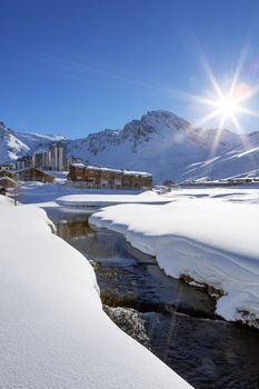 View of Tignes village with sun and creek, France.