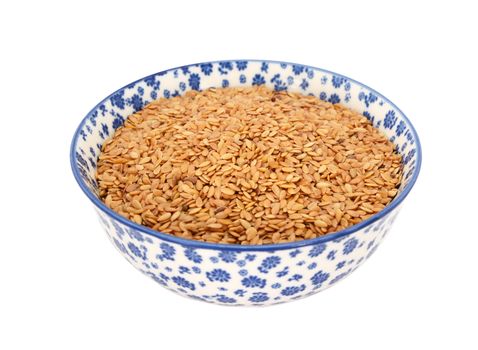 Golden linseed or flax seeds in a blue and white porcelain bowl with a floral design, isolated on a white background