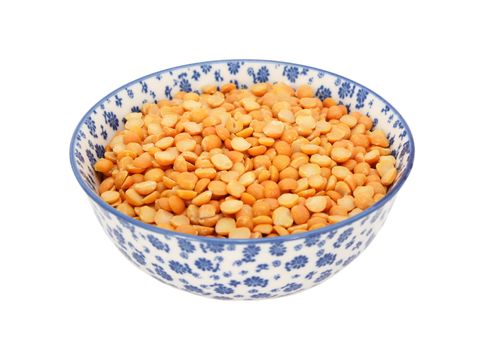 Yellow split peas in a blue and white porcelain bowl with a floral design, isolated on a white background