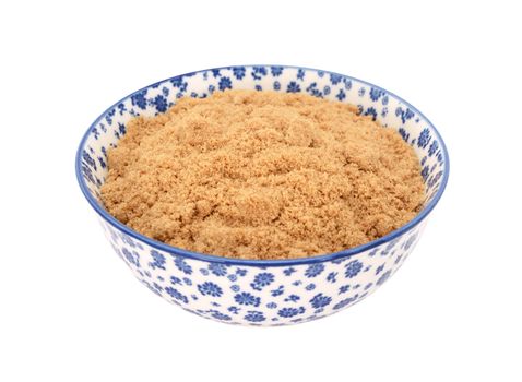 Light brown soft / muscovado sugar in a blue and white porcelain bowl with a floral design, isolated on a white background