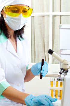 a female medical or scientific researcher or woman doctor looking at a test tube of dark solution in a laboratory