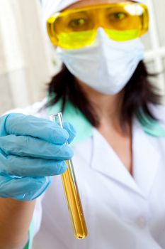 A female medical or scientific researcher or woman doctor shows a test tube of yellow solution in a laboratory