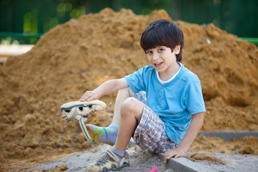 boy pours the sand out of the shoe on the playground
