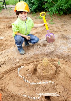 boy builder in a protective helmet and a shovel near the sand castle