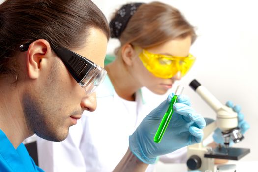 Male researcher analyzes tubes and his colleague looking through the microscope  