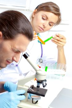 Female researcher analyzes tubes and his colleague looking through the microscope  