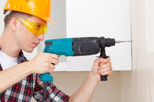 worker in protective helmet and goggles, is preparing to drill the wall