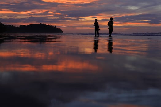 Silhouettes of two children on the beach during sunset