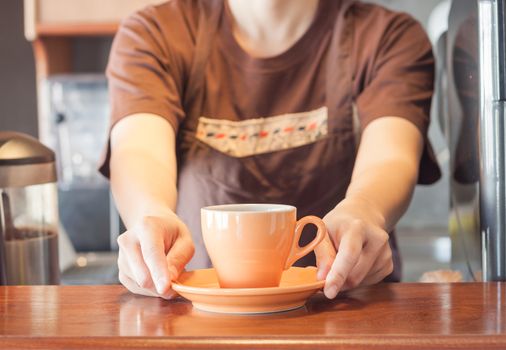 Barista offering orange cup of coffee, stock photo