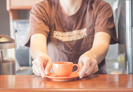 Barista offering mini orange cup of coffee, stock photo
