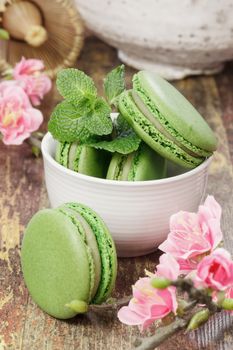 A teacup filled with matcha green tea macarons with cherry blossom over rustic background. Macro, selective focus