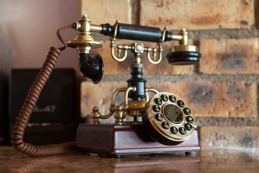 An antique analog telephone set with black box base and golden ringer, and handset
