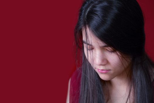 Beautiful, biracial teen girl looking down, depressed or sad, on red background