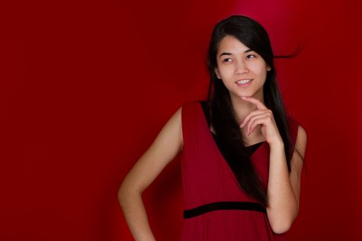 Beautiful biracial teen girl hand on chin thinking. Red background