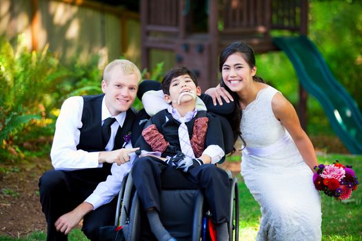 Biracial bride and groom with her little disabled brother in wheelchair on their wedding day