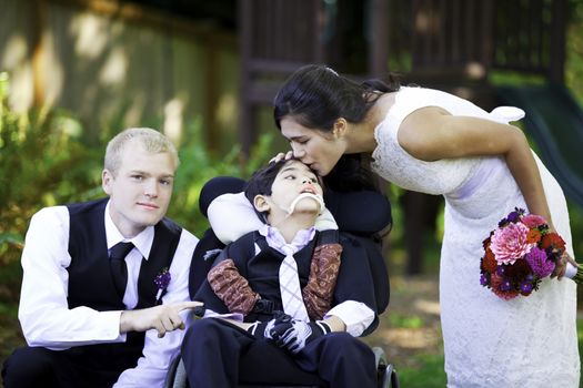 Biracial bride kissing her little brother on her wedding day. Child is disabled, in wheelchair