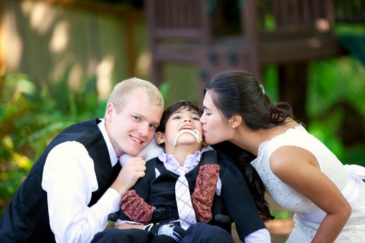 Biracial bride kissing her little brother on her wedding day. Child is disabled, in wheelchair