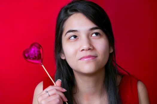 Beautiful biracial young teen girl holding heart balloon, smiling.